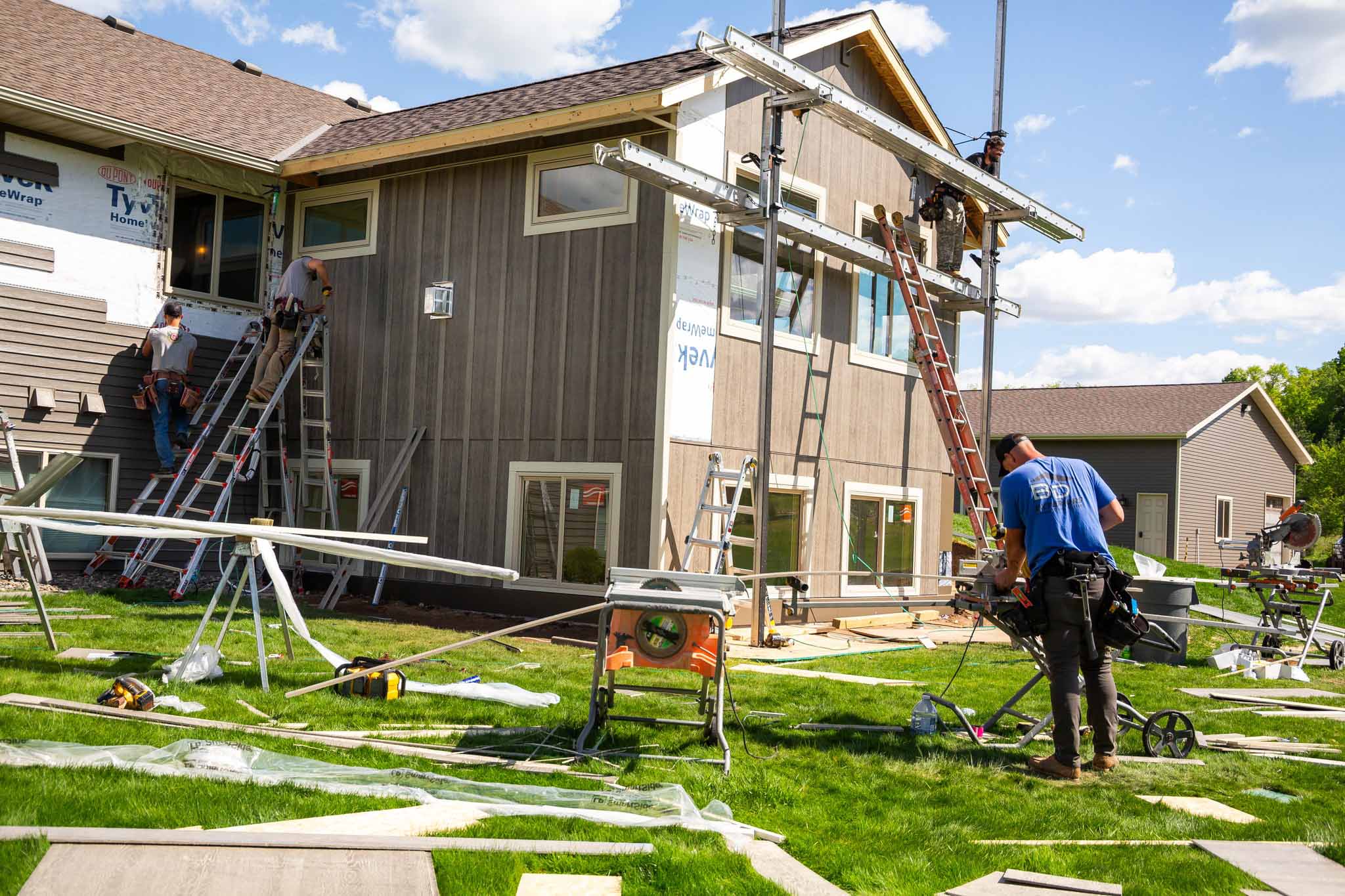 BD Exteriors team member cutting down siding panel with three other team members work on ladders and scaffolding