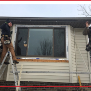 Two men installing new siding around a window during winter.