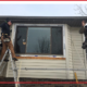 Two men installing new siding around a window during winter.